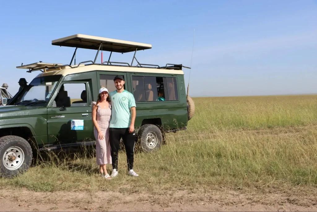 A couple posing next to a 4x4 safari vehicle on the Masai Mara plains.