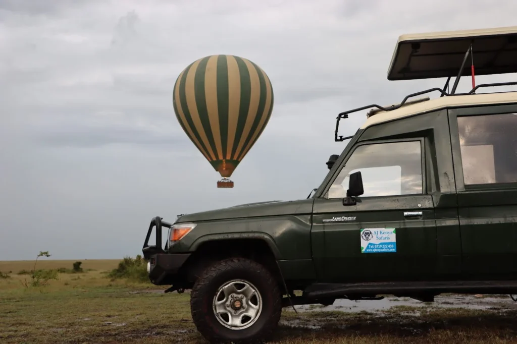 Safari vehicle and hot air balloon on savanna plains tracking zebras in Masai Mara.