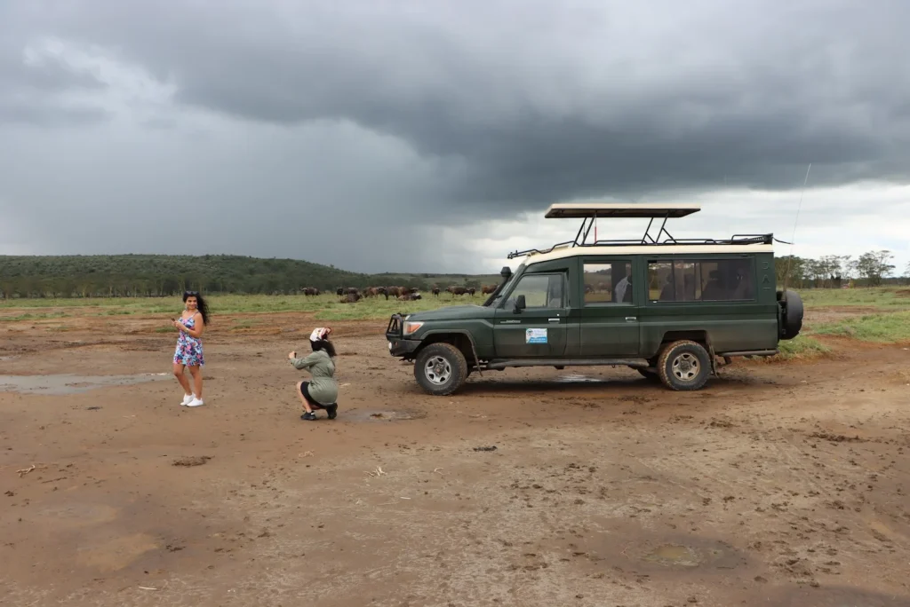 Tourists taking photos near a safari Land Cruiser under dramatic stormy clouds in Mara.