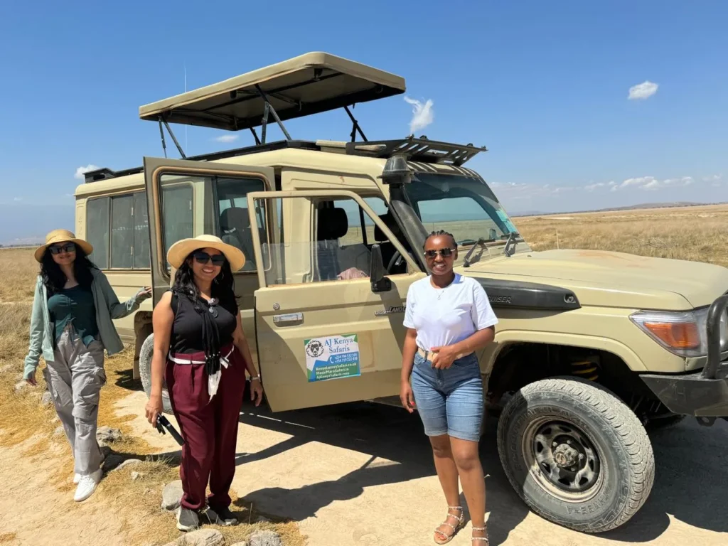 Three smiling tourists standing beside a 4x4 safari vehicle during a Kenya safari tour.