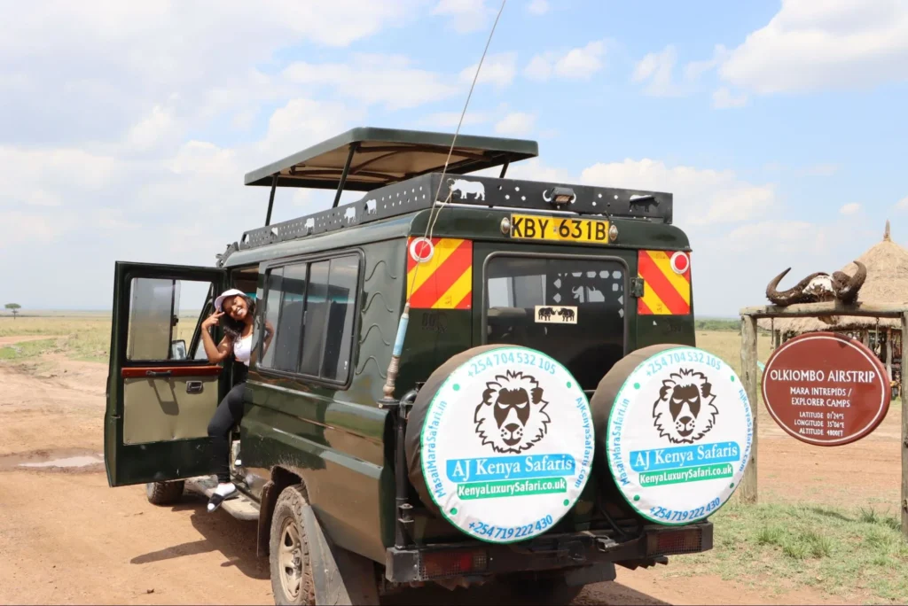 Tourist in a 4x4 safari land cruiser parked next to the Olkiombo Airstrip sign in the Masai Mara.