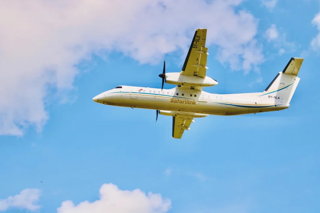 A white Safarilink airplane flying through a blue sky with light clouds.