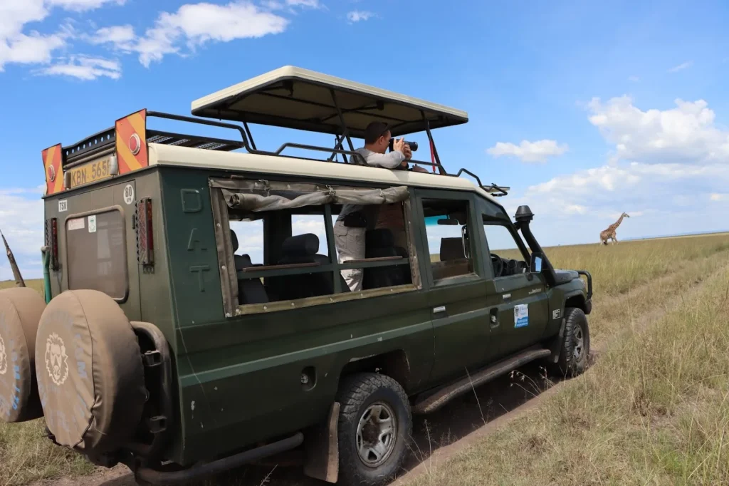 Tourists inside a 4x4 vehicle watching a distant giraffe in Masai Mara in December.