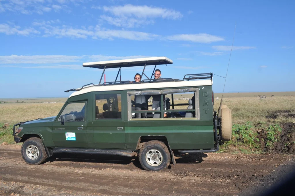A couple looking out from the open pop-up roof of a green 4x4 safari cruiser on a dirt track during a birding safari.