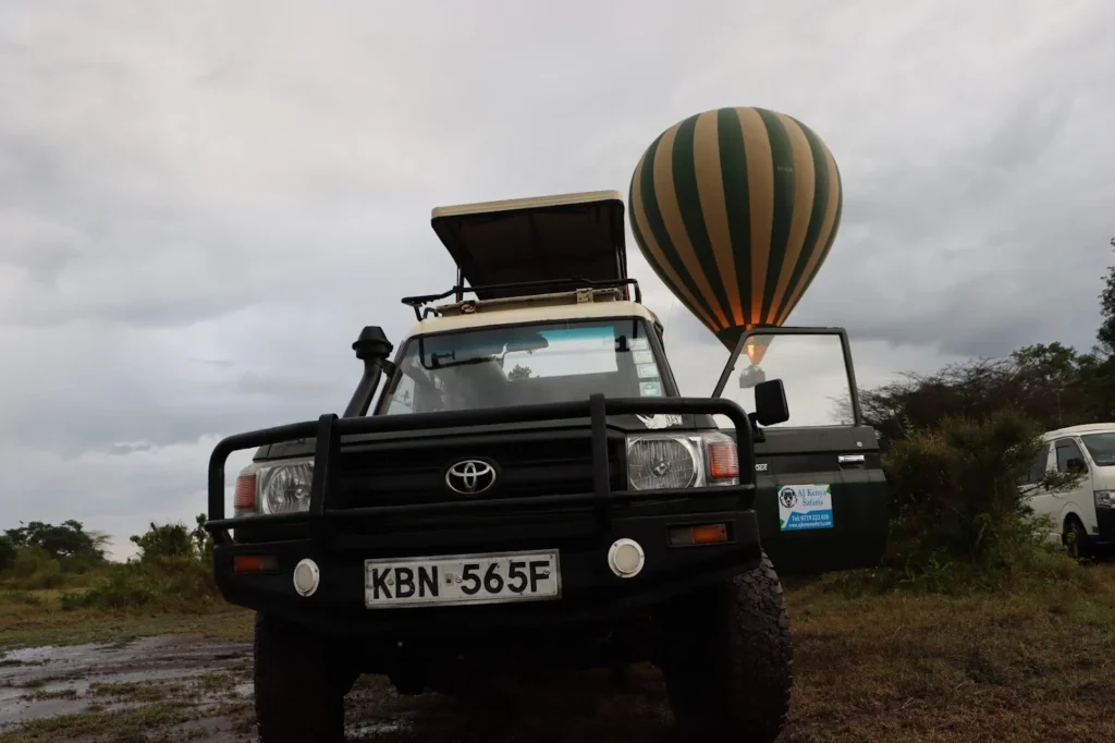A green 4x4 safari vehicle with a hot air balloon inflating behind it.