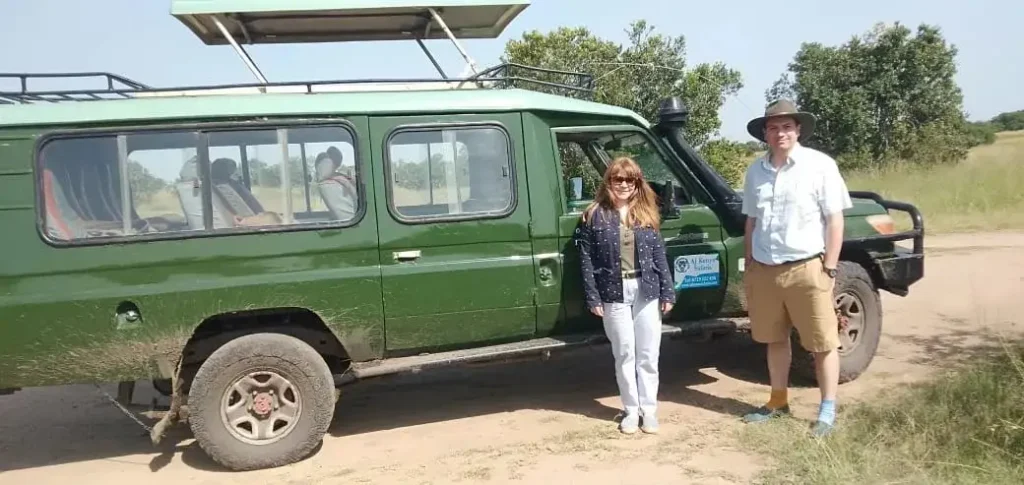 A couple standing next to a green 4x4 safari vehicle on a dirt track.