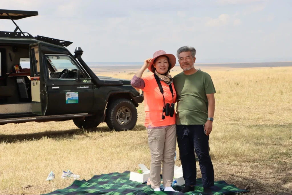 A happy couple standing near a 4x4 safari cruiser on a picnic break during their first time safari masai mara.