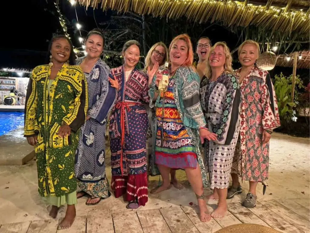 Women posing together in colorful patterned robes at an outdoor evening coastal resort.