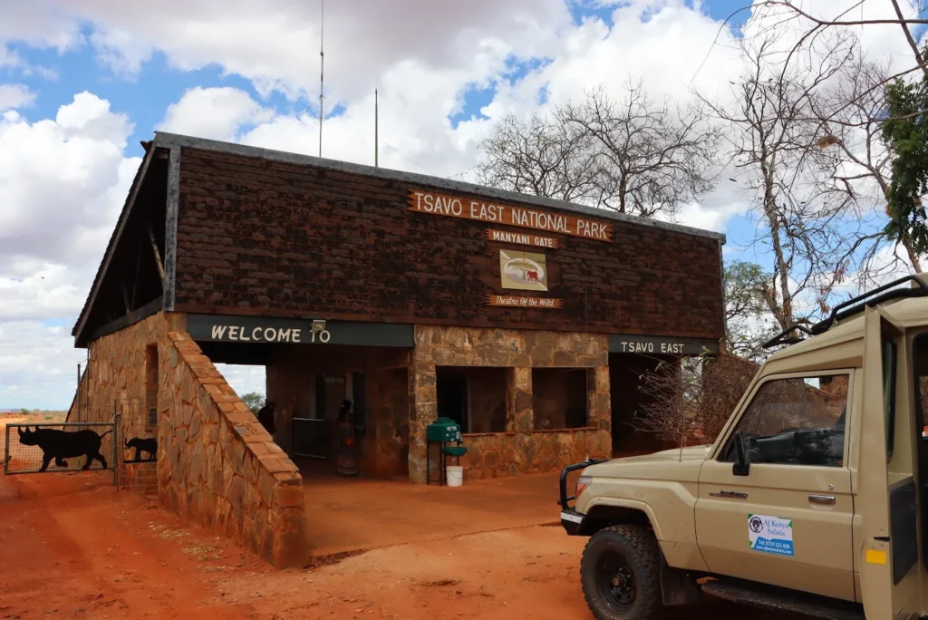 Safari vehicle parked outside the stone and wood Manyani Gate entrance at Tsavo East.