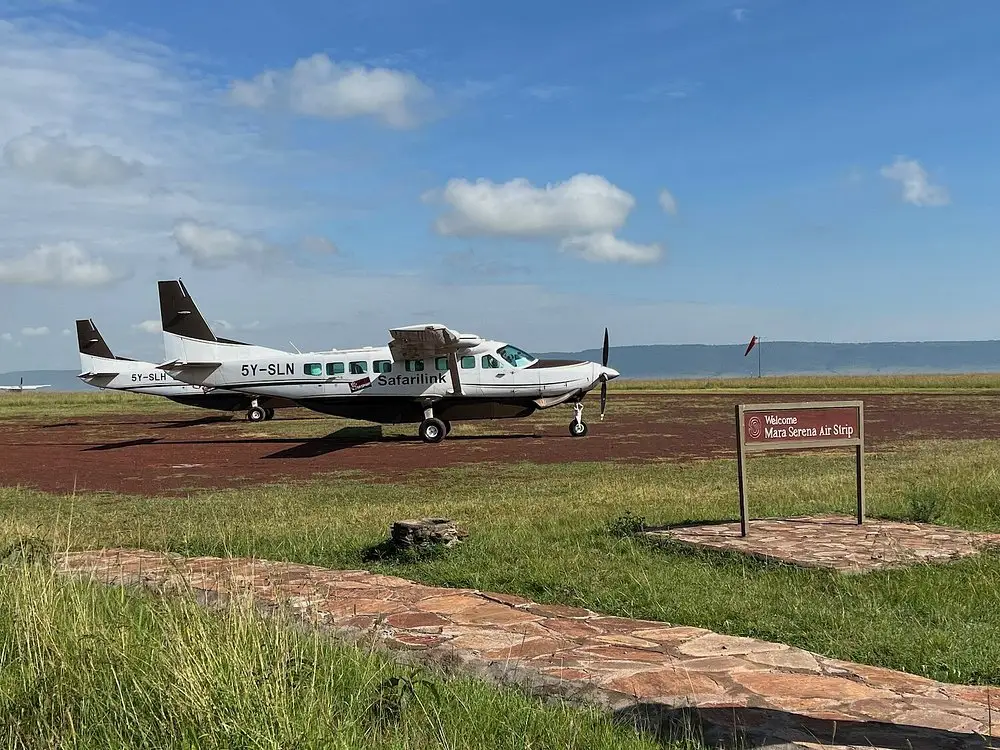Two small propeller airplanes parked on a dirt runway next to an airstrip sign.