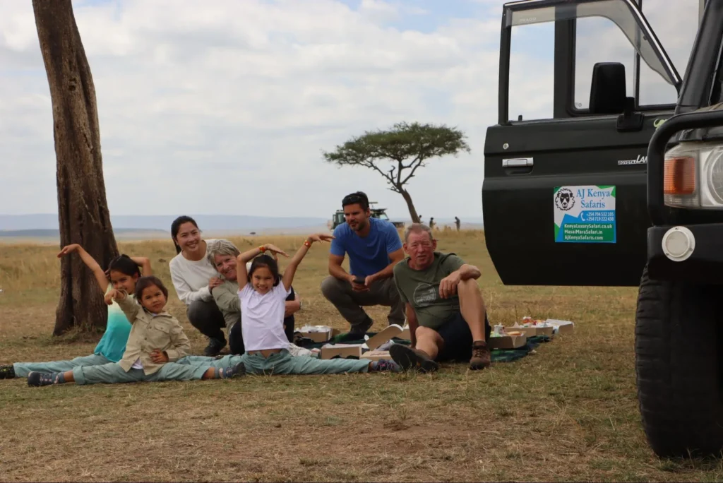A multi-generational family posing playfully during a bush picnic next to a safari vehicle.