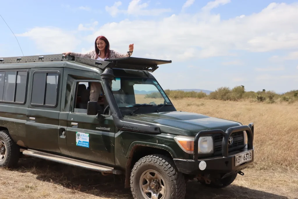 Woman standing through the open pop-up roof of a green safari Land Cruiser.