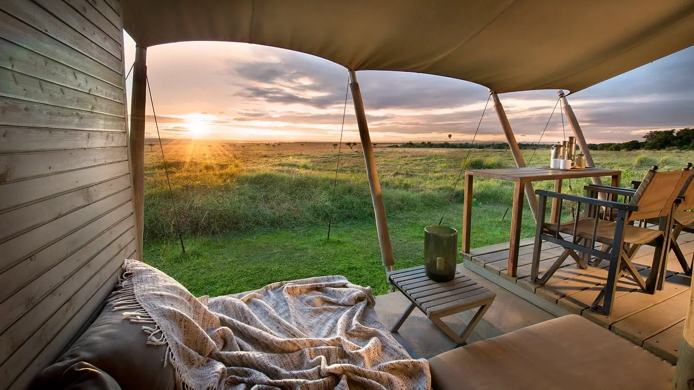 Open safari tent deck overlooking the grassy Masai Mara plains during a golden sunrise.