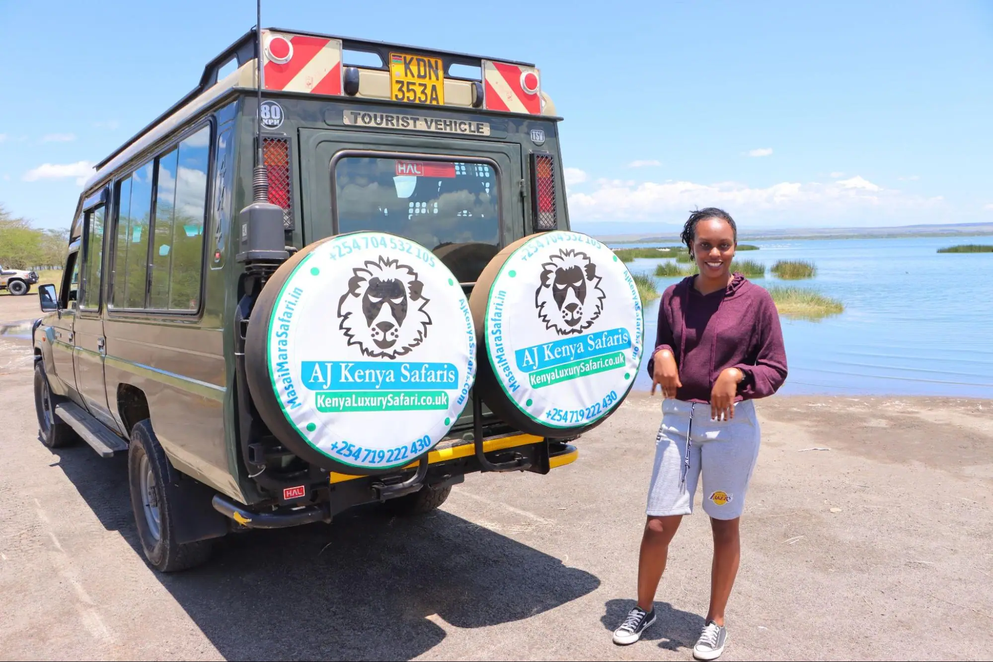 A woman standing next to a 4x4 safari vehicle with a lake backdrop.