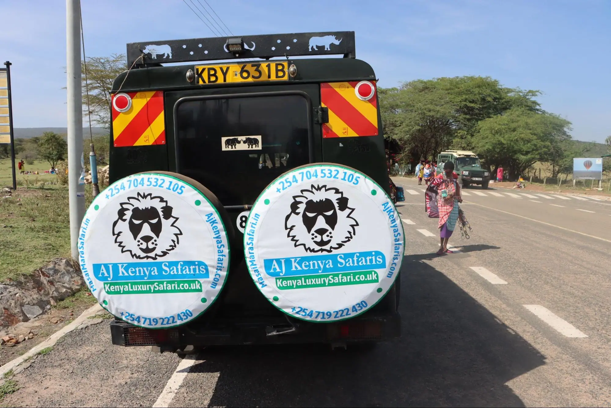 Rear view of a safari vehicle parked on a paved road with a Maasai person.