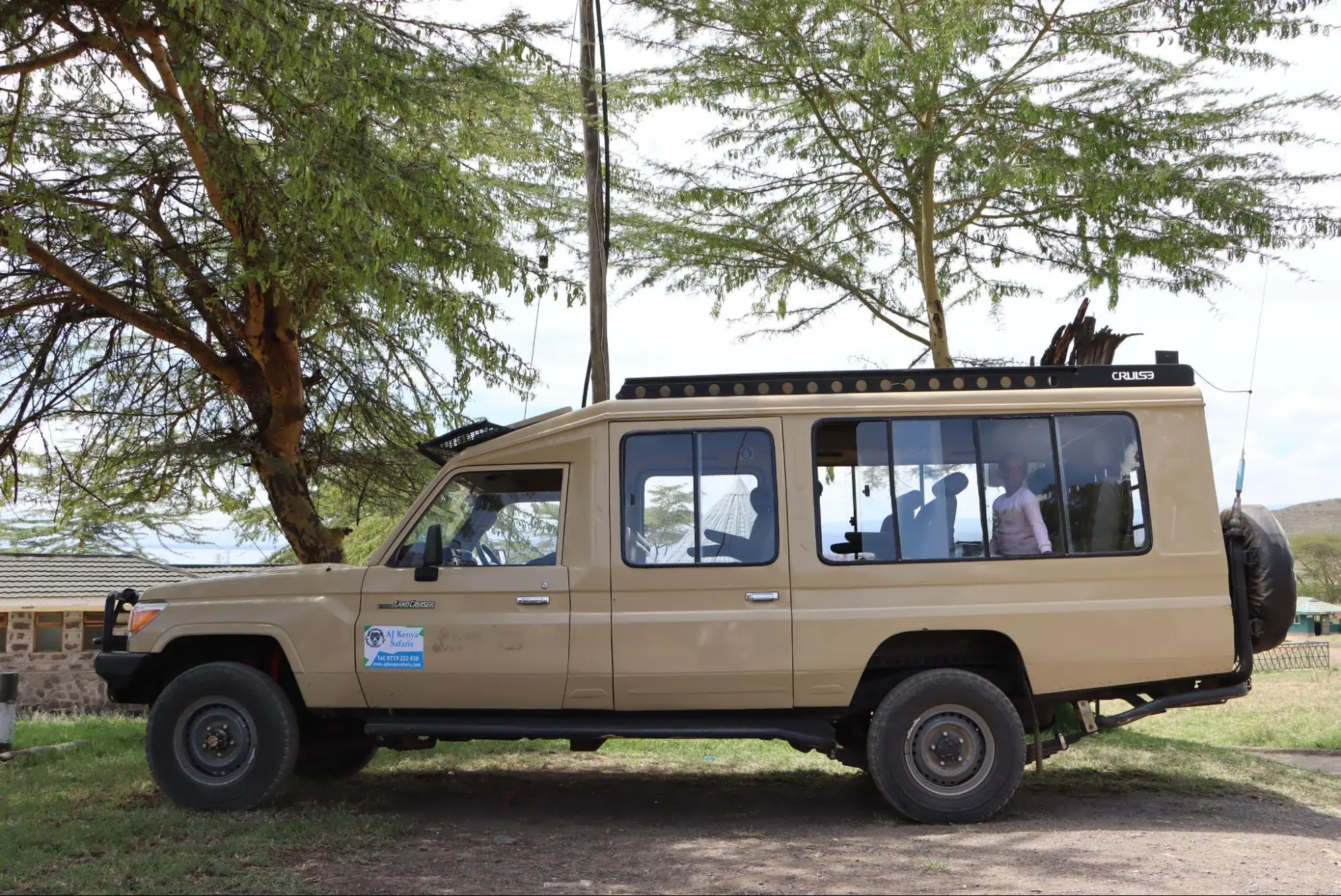Side view of a custom beige safari Land Cruiser parked under trees in Kenya.