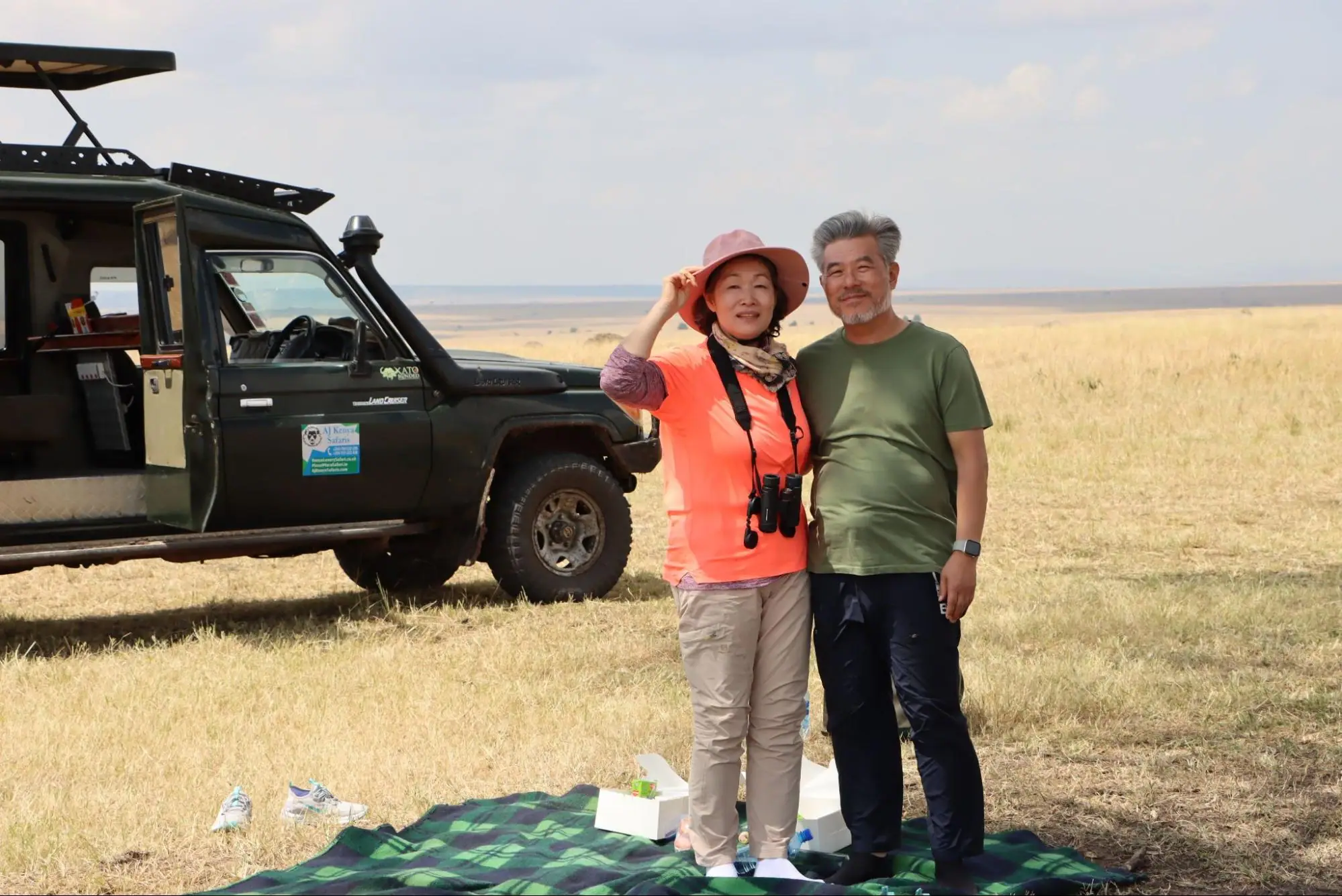 Happy couple standing by a safari vehicle during a bush picnic in Masai Mara.
