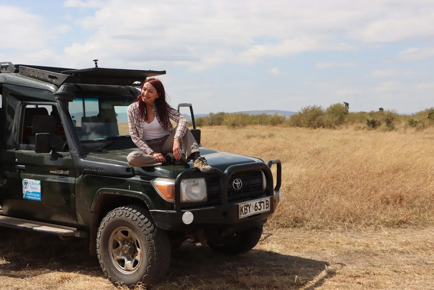 A woman sitting on the hood of a safari vehicle in the Kenyan savannah.