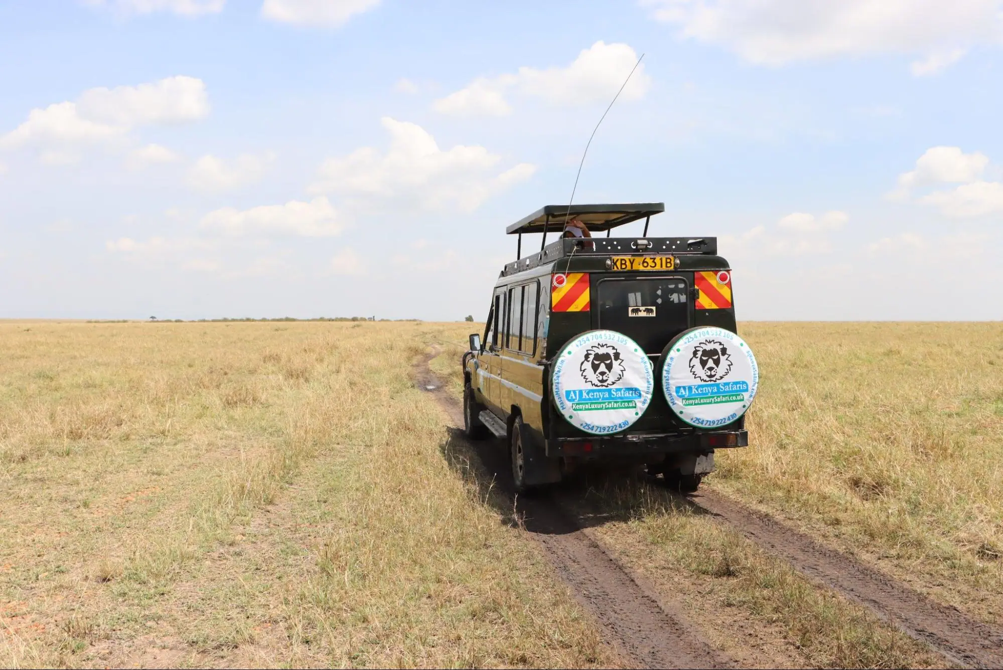 A safari Land Cruiser driving on a muddy track through the vast savanna.