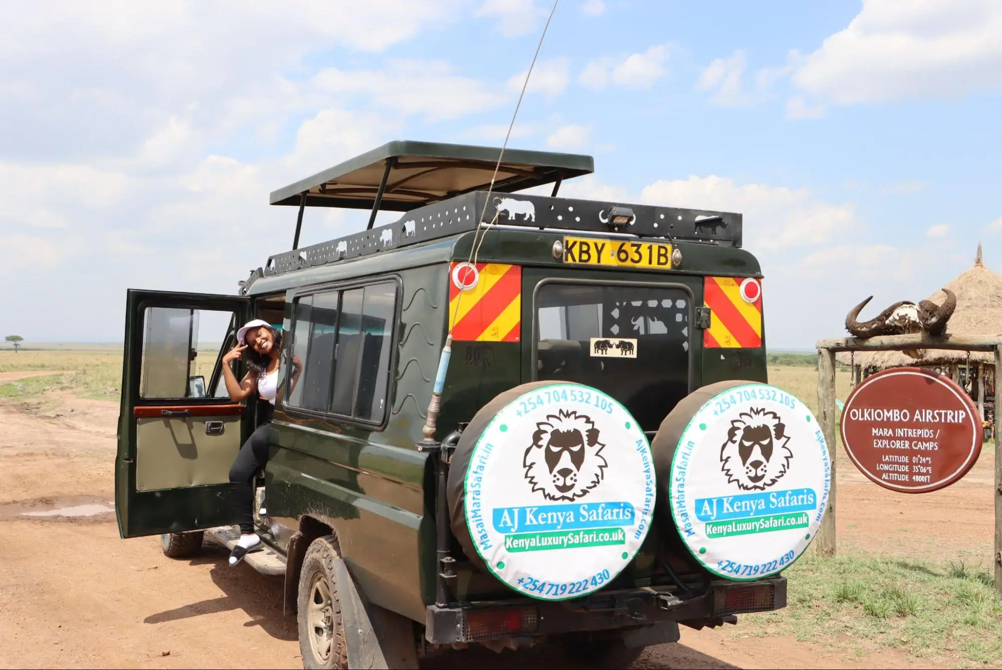 A young woman posing in a 4x4 safari vehicle next to Olkiombo Airstrip sign.
