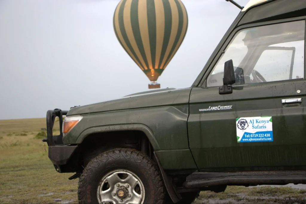 Green 4x4 safari Land Cruiser with a hot air balloon floating over the savannah.