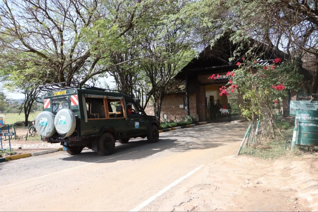 A green 4x4 safari vehicle driving through an arched brick entrance gate under shade trees.