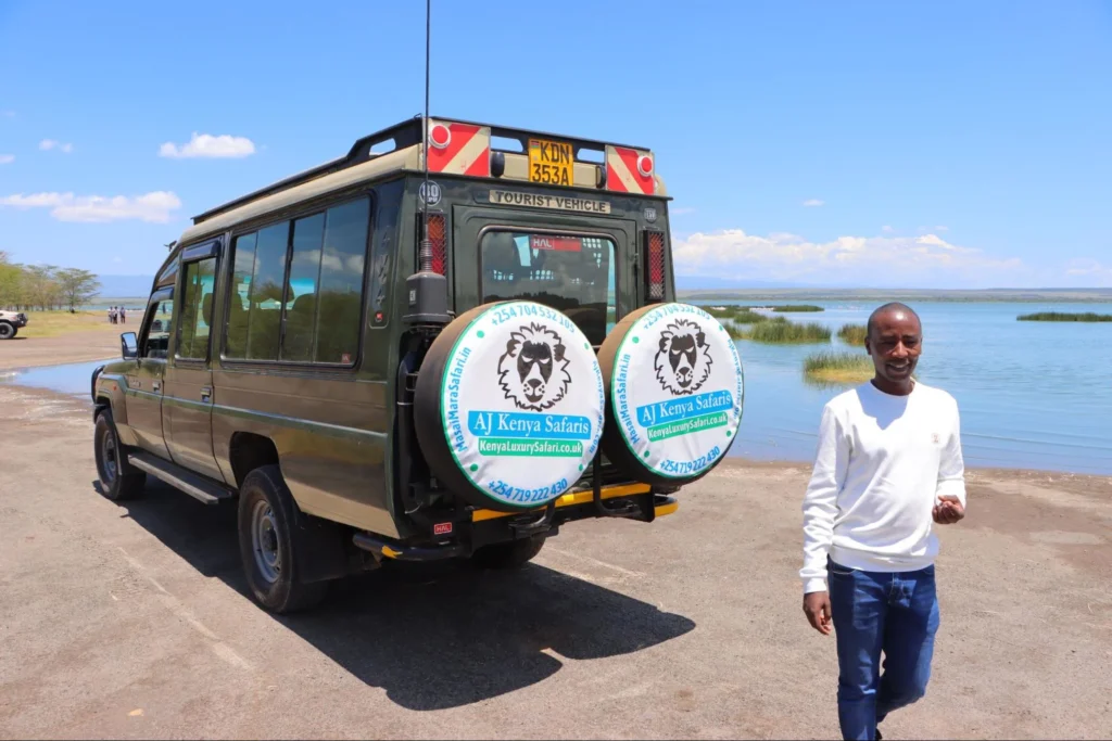 A man walking near a green 4x4 safari vehicle parked along a scenic shoreline.