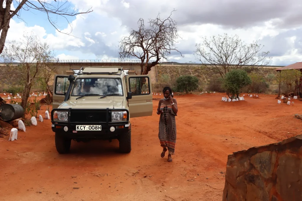 A beige 4x4 safari Land Cruiser parked on the vibrant red soil of Tsavo.