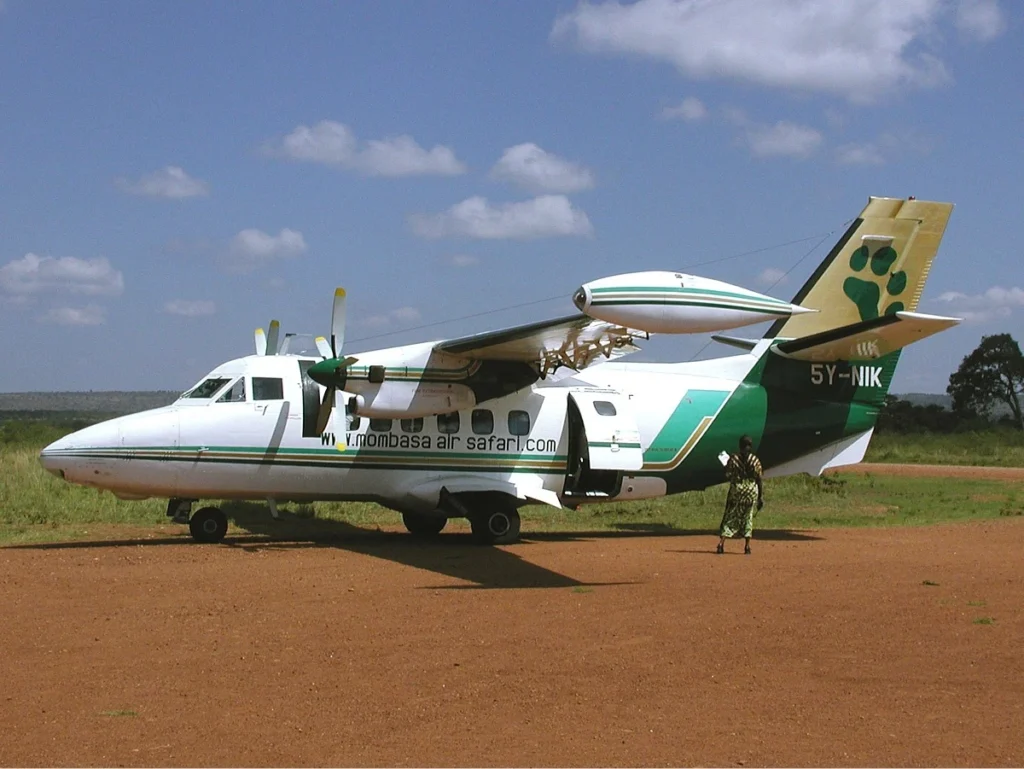 Twin-engine safari bush plane parked on a red dirt airstrip in the savannah.