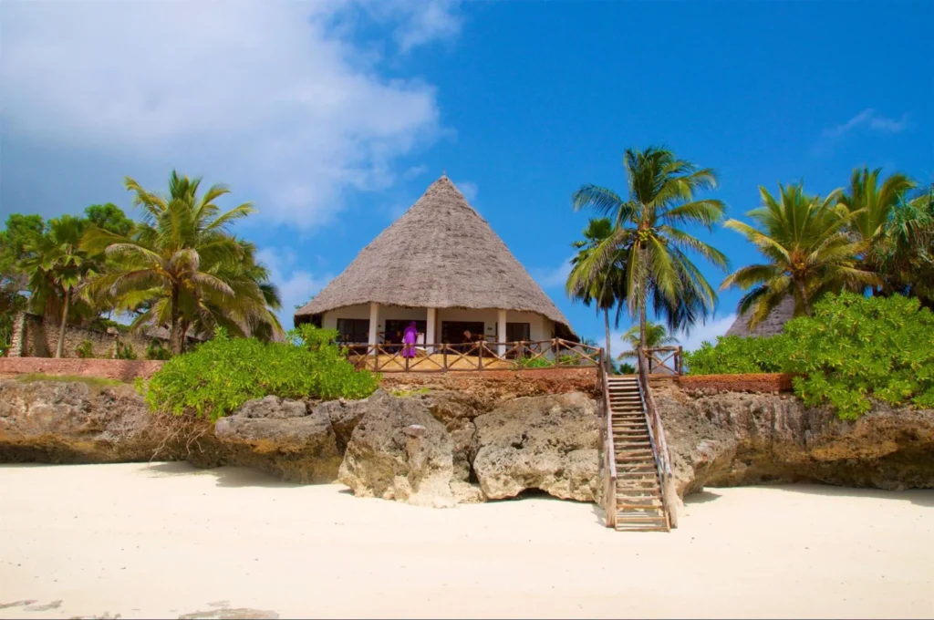 Thatched-roof beach bungalow on white sand under blue sky in Zanzibar.