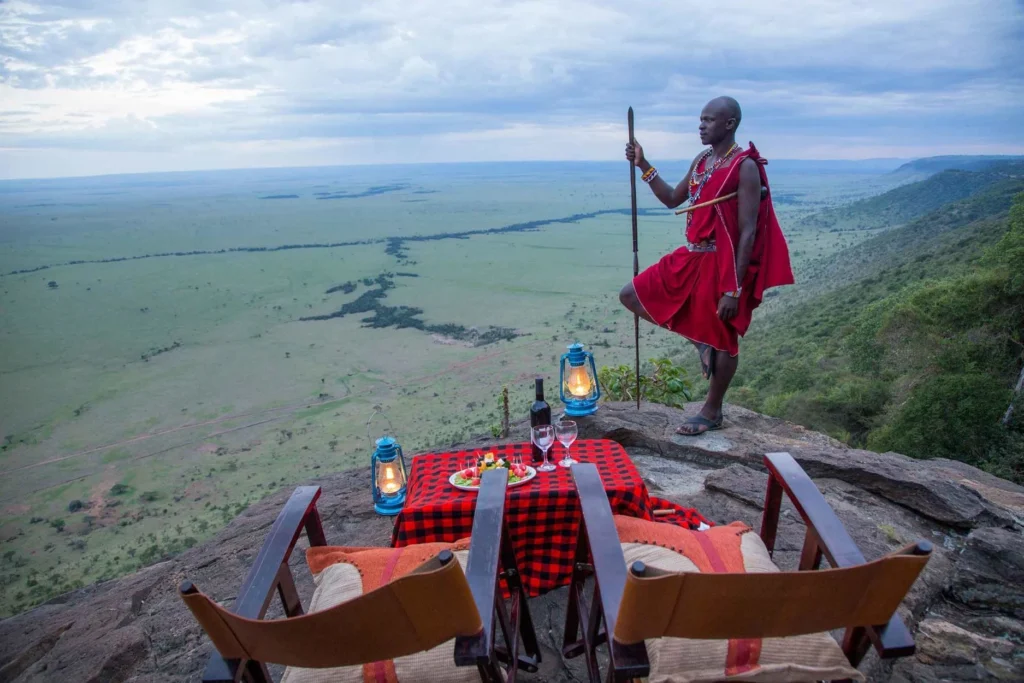 A Maasai warrior stands near a private sundowner setup at Mara Engai Wilderness Lodge.