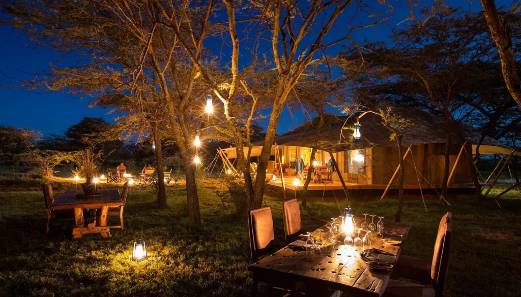 Outdoor night dining setup and luxury tents lit by lanterns at Mara Expedition Camp.