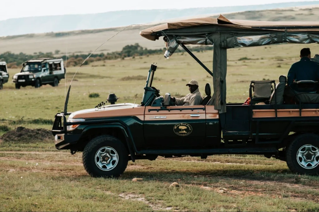 Mara Bush Camp open safari vehicle parked on the grassy savannah plains with hills behind.